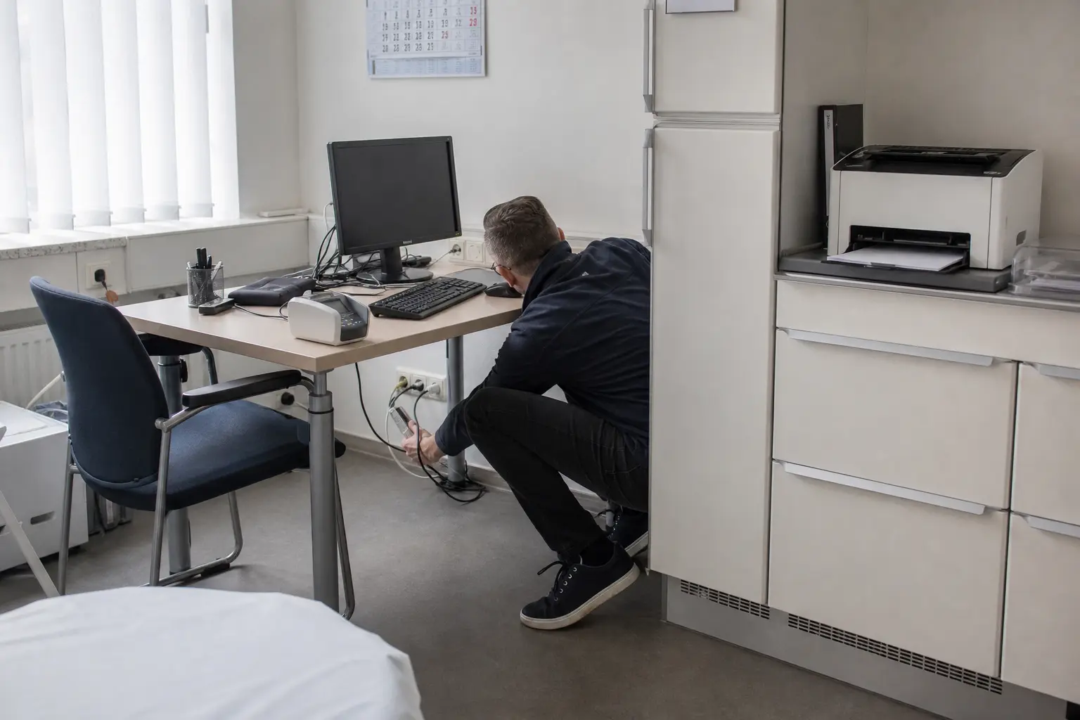 Techniker prüft die IT-Anschlüsse in einem leeren Behandlungsraum.